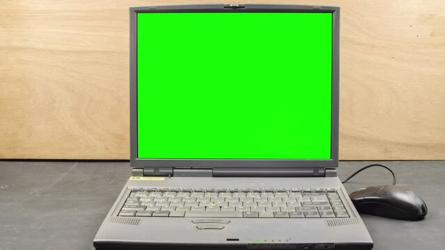 Lap top computer green screen ready for keying. Camera dolly mouse vintage IT old technology. Camera moving dolly. 90's workspace computer laptop on a black table, wood grain background vintage old IT