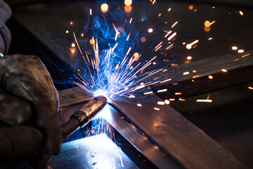Closeup photo of metalworking in dark workshop. Welding and grinding with lot of sparks and smoke