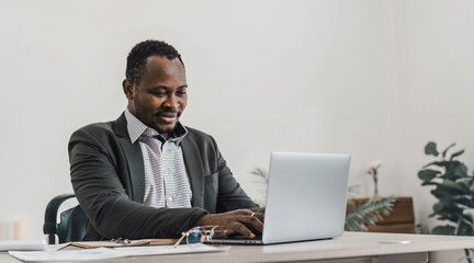 Focused african american businessman working with laptop documents in office holding papers preparing report analyzing work results, black male analyst doing paperwork at workplace using computer