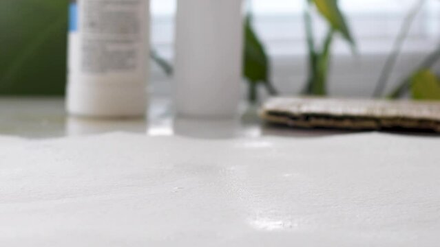 Close up diverse female artist prepping and priming white cotton rag paper by misting water with spray bottle, then blobbing on white clear gesso then using wide artist brush