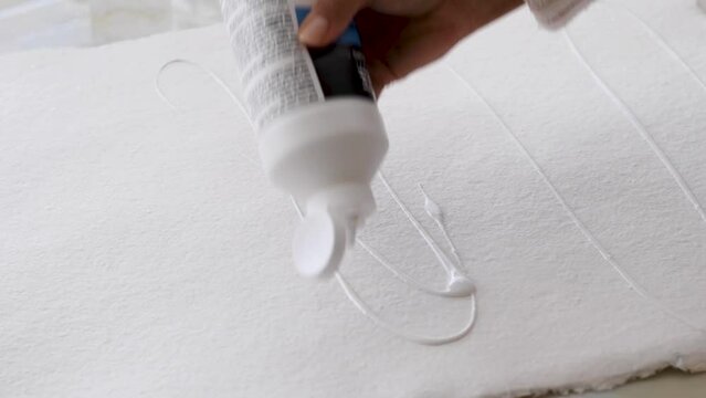 Close up diverse female artist prepping and priming white cotton rag paper by blobbing on white clear gesso then using wide artist brush