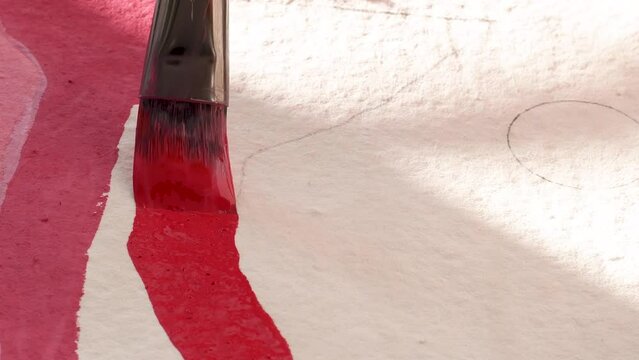 A female artist painting with a paint brush on cotton rag paper with acrylic gouache in red on a colourful bold work with organic shapes with sun shining on paper