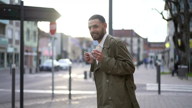 One Happy Arab man dancing in celebration outside in city street while walking toward camera. A Middle Eastern male person wearing jacket celebrates success