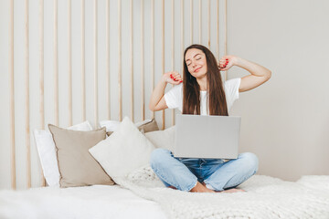 student girl woke up stretches and sits with a laptop on the bed going to work online