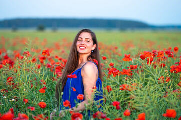 Obraz na płótnie Canvas pretty young woman with long hair playing with petals in poppy field in evening sunlight