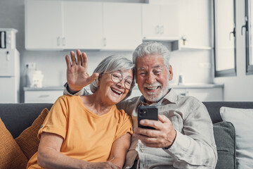Happy retired family couple using mobile phone for video call together, talking to relations, getting good news, having fun, smiling and laughing. Carefree mature pensioners chatting online on cell.