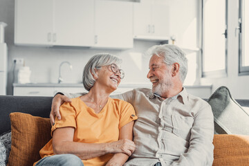 Happy laughing older married couple talking, laughing, standing in home interior together, hugging...