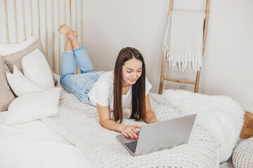 Obraz premium Girl advertising manager works at home with a laptop lying on a white bed