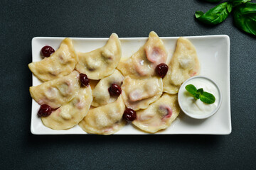 Dumplings with cherry and sour cream on a white square plate. Free space for text. On a dark background.