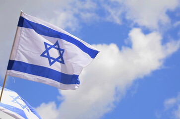 Flag of Israel against a bright blue sky. Star of David on a white background.