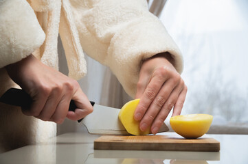 Obraz na płótnie Canvas housewife cuts raw potatoes into small pieces with a knife. Close-up of a woman's hands in a bathrobe while working in the kitchen. Cooking delicious breakfast or dinner