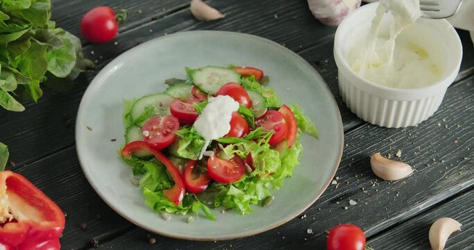 Putting stracciatella cheese on top of salad in plate. Italian stretched cheese in bowl, person eating mozzarella cheese with fork, healthy salad with leaves and tomato cherries, 4k video footage