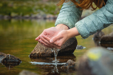 Close-up of a woman's hand pouring water from her palms while trying to drink from a clean water...