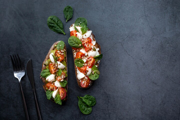 Bruschetta (sandwiches) with cherry tomatoes, mozzarella cheese and herbs on a dark background. A traditional Italian snack.
