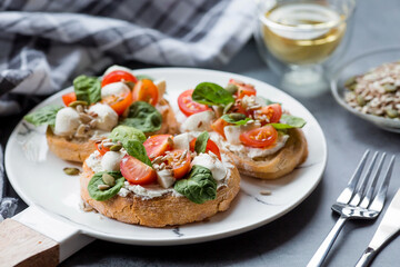 Bruschetta (sandwiches) with cherry tomatoes, mozzarella cheese and herbs on a stylish plate on a dark background. A traditional Italian snack.