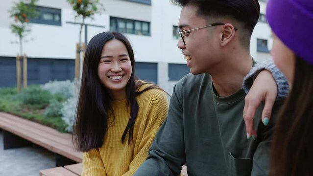Asian young adult people having fun while social gathering on city park. Millennial ethnic friends laughing and enjoying time together outdoors.