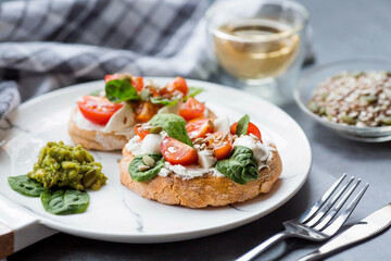 Bruschetta (sandwiches) with cherry tomatoes, mozzarella cheese and herbs on a stylish plate on a dark background. A traditional Italian snack.