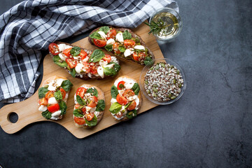 Bruschetta (sandwiches) with cherry tomatoes, mozzarella cheese and herbs on a cutting board on a dark background. Traditional Italian snack.