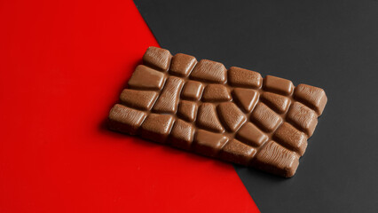 Whole rectangular bar of chocolate on a diagonal red and black background.