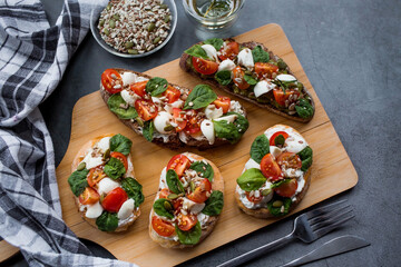 Bruschetta (sandwiches) with cherry tomatoes, mozzarella cheese and herbs on a cutting board on a dark background. Traditional Italian snack.