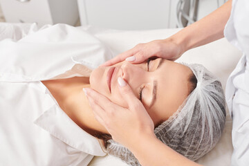 Cosmetologist massages woman face skin after rubbing moisturizing cream for rejuvenation, anti...