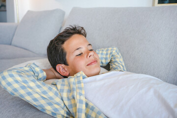 Relaxed boy resting lying on a couch with the hands on the head at home