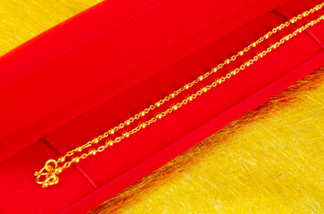 The Gold Necklace in red velvet box container on gold color background.