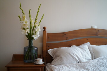 Bedroom closeup view. Spring blooming branch, white flowers on the bedside table, cup of tea or coffee and white bedding sheets. Spring, light, calmness, coziness.
