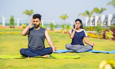 Young couple doing yoga or pranayama with eyes closed during morning at park - concept of healthy lifestyles, mindfulness and morning rituals