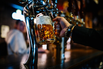 man bartender hand at beer tap pouring beer in glass in bar or pub