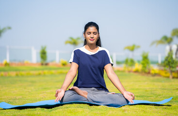 Young woman doing yoga or meditation with eyes closed at park - concept of relaxation, self care...