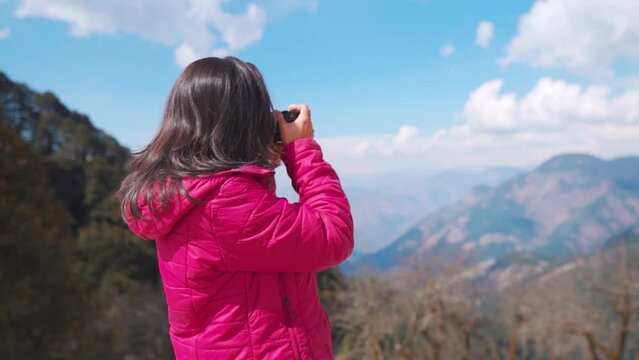 Confident Indian female photographer taking photographs of mountains with her camera at Jalori Pass, Himachal Pradesh, India. Rack focus. Young female photographer with digital SLR camera in mountains
