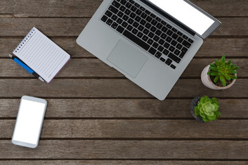 Laptop, pot plant, notepad, pen and mobile phone on wooden plank