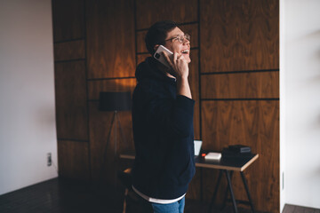 Cheerful young man talking on smartphone in living room