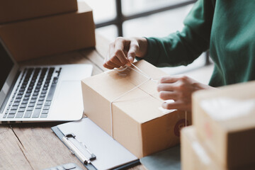 An woman tying a parcel to a customer's box, she owns an online store, she packs and ships through a private transport company. Online selling and online shopping concepts.