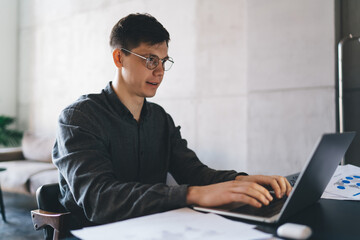 Fototapeta premium Positive man typing on laptop in office