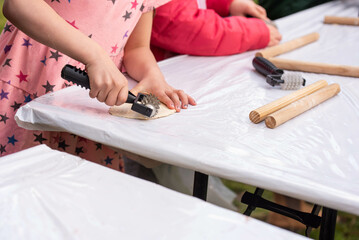 Kids cooking, roll out the dough and making matzah for Jewish holiday Passover Pesach at culinary master class for children outdoor in park. 