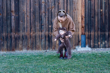 Woman holding baby in her hands. Mother and son playing against 	wooden wall.