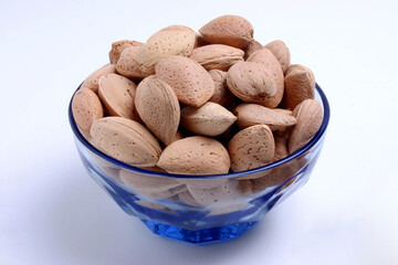 Inshell almonds in a blue bowl with white background.