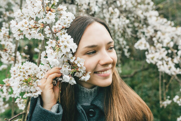 A young beautiful smiling girl stands near a flowering tree in the garden. Spring concept