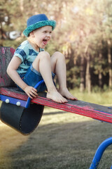 A little cheerful boy in blue clothes is sitting high on a balance swing and is very happy.