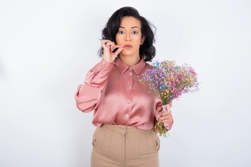 young woman holds big bouquet of nice flowers over white background mouth and lips shut as zip with...