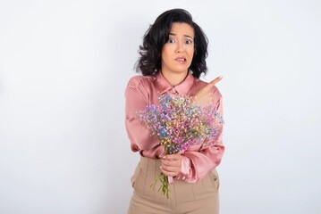 young woman holds big bouquet of nice flowers over white background Pointing aside worried and...