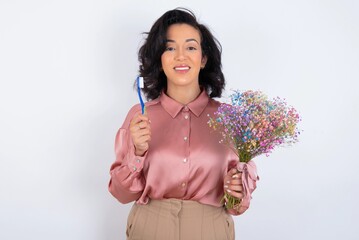 young woman holds big bouquet of nice flowers over white background holding a toothbrush and smiling. Dental healthcare concept.