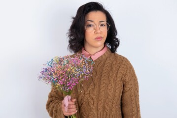Displeased young woman holds big bouquet of nice flowers over white background frowns face feels...
