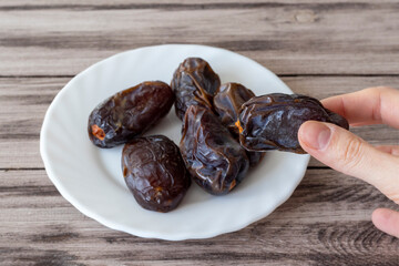 A large royal date in a woman's hand against a plate of dates