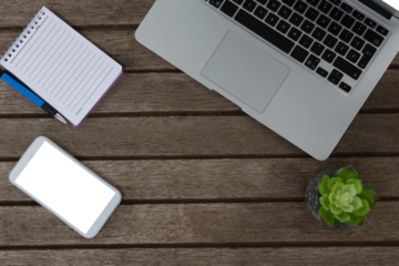 Laptop, pot plant, notepad, pen and mobile phone on wooden plank