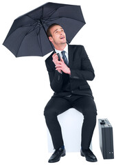 Smiling businessman under umbrella sitting on cube