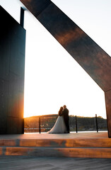 The newlyweds pose against the background of a modern arch in the evening