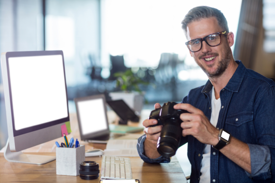 Portrait of man holding digital camera by desk